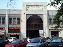 Fachada principal del mercado con coches aparcados y árboles en primer plano