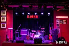Escenario vacío del La Movida Café Concierto con iluminación púrpura y equipo musical listo para el show