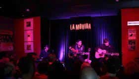 Concierto en vivo en La Movida Café Concierto con banda tocando bajo luces rojas y público presente