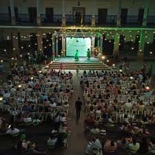 Escenario iluminado con luces verdes en el patio interior del venue, rodeado de asistentes