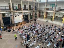 Configuración del escenario con pantalla y sillas blancas dispuestas para un evento al aire libre