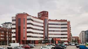 Fachada exterior del hotel durante el día con estacionamiento frente al edificio