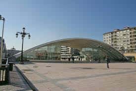 Fachada exterior de la estructura arqueada de la plaza bajo cielo despejado, con peatones transitando