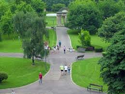 Entrada principal del parque con senderos arbolados y personas caminando