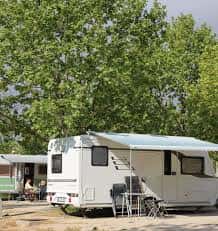 Caravana estacionada bajo árboles frondosos con zona de descanso