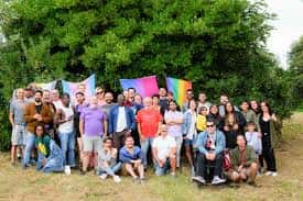Grupo de personas reunidas en un entorno natural con banderas del orgullo LGBTQ+
