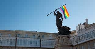 Estatua en plaza pública con bandera del orgullo LGBTQ+ ondeando en el cielo azul