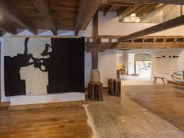 Interior de la galería con vigas de madera y una gran obra de arte abstracta en la pared