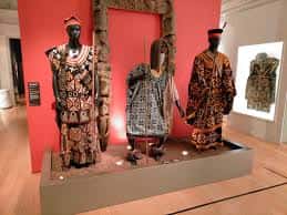 Exposición de trajes y figuras talladas en una sala con fondo rojo