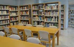 Sala de lectura con mesas largas y sillas blancas rodeadas de estanterías de libros
