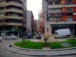 Plaza con monumento en el centro de la calle Río de la Pila, rodeada de edificios y tráfico