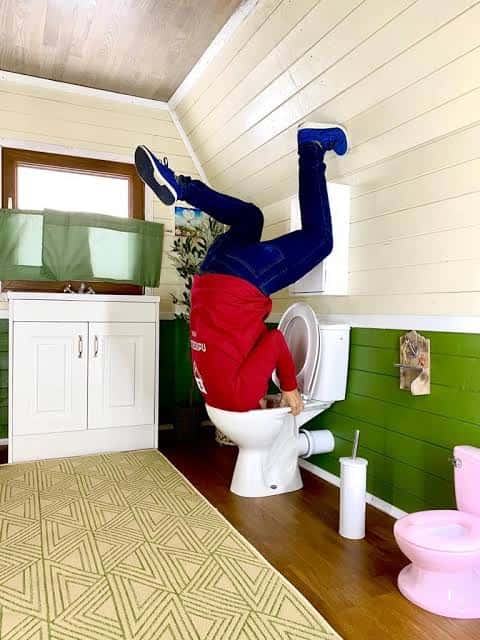 Baño invertido con persona colgando sobre el inodoro
