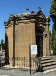 Capilla funeraria de estilo tradicional con cruz en la fachada y reja perimetral
