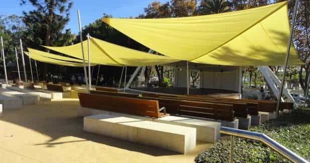 Interior del auditorio con toldos amarillos y asientos de madera bajo la luz del día