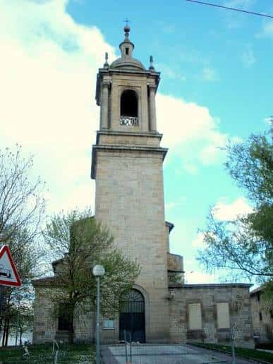 Fachada frontal de la iglesia con entrada principal y torre bajo cielo azul