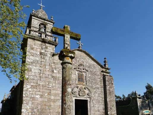 Vista exterior de la Iglesia de Santo André de Xeve con su fachada de piedra y cruz en primer plano