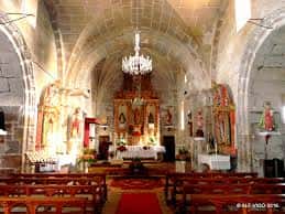 Vista del interior de la iglesia con bancos de madera, altar adornado y luz natural entrando por ventanas laterales