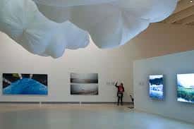 Espacio expositivo con instalación artística suspendida y obras en pared