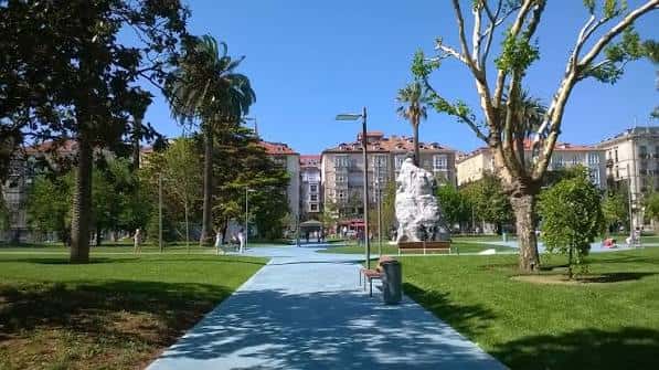 Paseo central con césped, palmeras y escultura blanca en el corazón del jardín