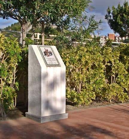 Monumento conmemorativo blanco rodeado de vegetación en el parque