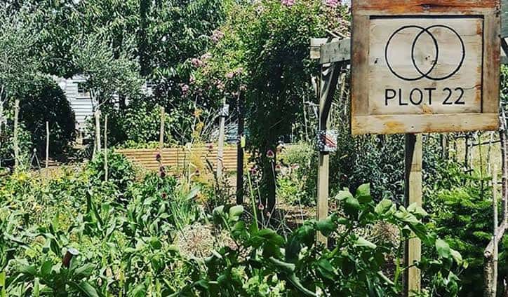 Entrada del jardín comunitario Plot 22 con letrero de madera y vegetación exuberante