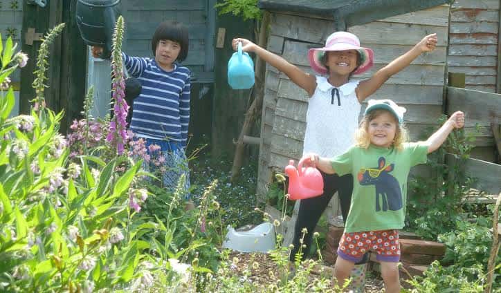Niños jugando con regaderas en un huerto comunitario lleno de flores