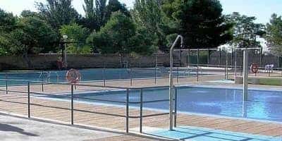 Piscina al aire libre del centro deportivo con zona de madera y árboles al fondo