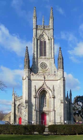 Fachada principal de St Peter's Church con torre gótica y puertas rojas bajo cielo azul