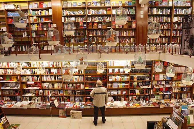 Vista panorámica del interior de la librería con estanterías llenas y jaulas decorativas colgantes