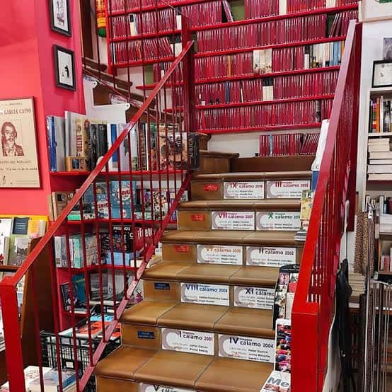 Escalera roja con libros en los escalones y estanterías de fondo
