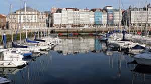 Puerto deportivo de A Coruña con veleros amarrados y fachadas urbanas reflejadas en el agua