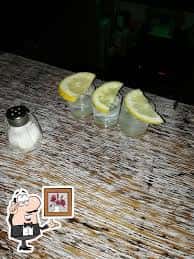 Vista cenital de tres shots de tequila con rodajas de limón sobre una barra de madera
