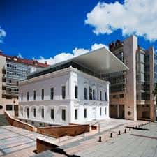 Vista exterior del edificio del Colegio Oficial de Arquitectos de Asturias en Oviedo, con fachada clásica y ampliación moderna bajo cielo azul