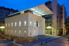 Fachada iluminada del edificio del Colegio Oficial de Arquitectos de Asturias al atardecer, mostrando contraste entre arquitectura histórica y contemporánea