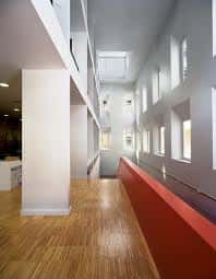 Interior del edificio con pasillo luminoso, suelo de madera y pared roja, ideal para eventos culturales o exposiciones