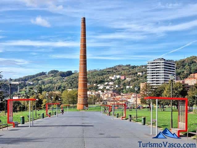 Chimenea histórica del parque rodeada de áreas verdes y estructuras rojas