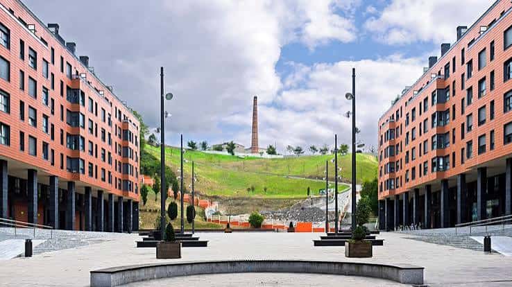 Plaza central entre edificios modernos con la chimenea al fondo