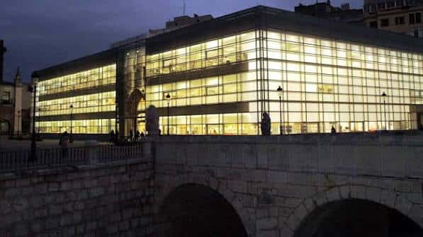 Vista nocturna de la biblioteca desde el puente, mostrando su fachada de cristal iluminada