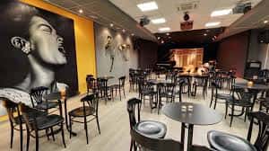 Interior del espacio de Clasijazz con mesas y sillas dispuestas para eventos, y gran mural de artista de jazz en la pared