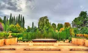 Escenario del teatro rodeado de jardines y cipreses bajo cielo nublado
