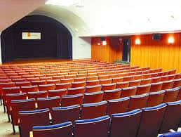 Interior del auditorio con butacas rojas y escenario con cortinaje azul