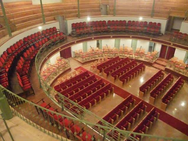 Interior del teatro con butacas rojas dispuestas en forma de herradura y escenario con telón decorado