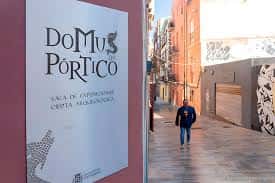 Vista exterior de la fachada rosa de la Sala de Exposiciones Domus del Pórtico con cartel informativo