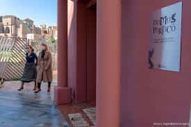 Entrada lateral de la Domus del Pórtico con dos personas caminando junto a la pared rosa