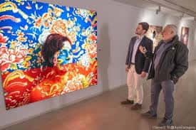 Interior de la sala con una gran obra de arte colorista y visitantes observando la exposición