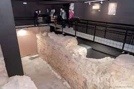 Vista general del espacio expositivo con las ruinas arqueológicas y visitantes en la pasarela