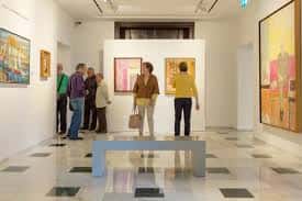Interior de la sala de exposiciones con visitantes y obras colgadas