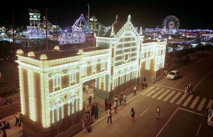 Vista aérea del recinto ferial de noche con la entrada iluminada y atracciones al fondo