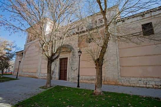 Fachada lateral del monasterio con árboles y puerta de acceso