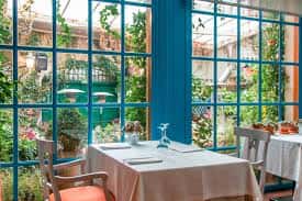 Sala interior con mesas dispuestas para banquete y grandes ventanales con vistas a un jardín